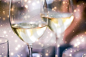 Winter holiday glasses of white wine and glowing snow on background, Christmas time romance