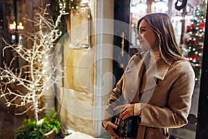 Winter holiday season. Christmas, New Year concept. Woman waiting for friends by illuminated showcase on city street.