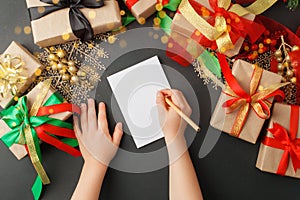 Winter Holiday Season. Top view of kid hands making Christmas Letter for Santa Claus on natural shades of green background, xmas,