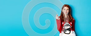 Winter holidays and Christmas Eve concept. Lovely redhead woman in xmas sweater, showing heart sign and thinking