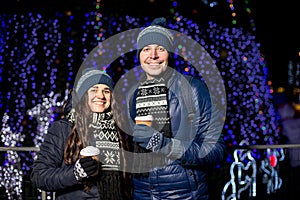 Winter holidays, hot drinks and people concept - happy young couple with coffee at christmas market in evening