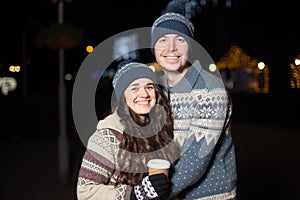 Winter holidays, hot drinks and people concept - happy young couple with coffee at christmas market in evening