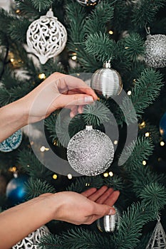 Winter holidays and people concept - close up of young woman hands decorating christmas tree with red ball over snow