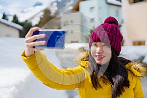 Winter holidays in Swiss Alps - young beautiful and happy Asian Chinese woman  taking selfie with mobile phone on snow landscape