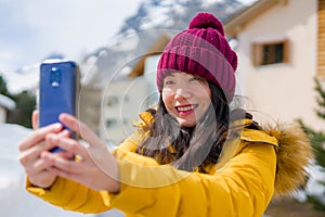 Winter holidays in Swiss Alps - young beautiful and happy Asian Korean woman  taking selfie with mobile phone on snow landscape
