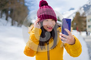Winter holidays in Swiss Alps - young beautiful and happy Asian Korean woman  taking selfie with mobile phone on snow landscape