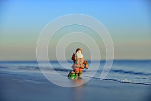 Winter on hot beach. Christmas holiday concept. Toy santa on the sea.