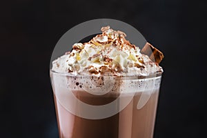 Winter hot chocolate cocoa drink in tall glass with ispices and whipped cream on black table. Dark blue background. Copy space