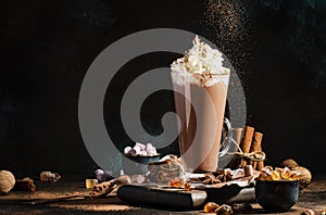 Winter hot chocolate cocoa drink in tall glass with ispices and whipped cream on black table. Dark blue background. Copy space