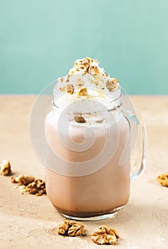 Winter hot dark chocolate or cocoa drink with whipped cream and crushed walnuts in glass jar, beige table, copy space