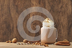 Winter hot dark chocolate or cocoa drink with whipped cream and crushed walnuts in glass jar, wooden table, copy space