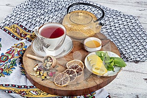 Winter hot tea with fruit, berries and spices in a cup on a table seen with cast iron teapot and herbs and dried fruits