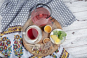 Winter hot tea with fruit, berries and spices in a cup on a table seen with cast iron teapot and herbs and dried fruits