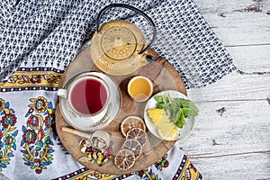 Winter hot tea with fruit, berries and spices in a cup on a table seen with cast iron teapot and herbs and dried fruits