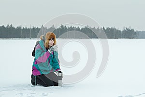 Winter hunkering hiker woman drinking hot tea from vacuum flask metal cup