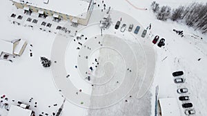A winter ice rink filmed by a drone on a sunny frosty day. Children and adults, hockey players skate on the ice.