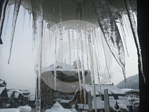 Winter icicles on a window frame with beautiful view of a mountain forest from a ski resort