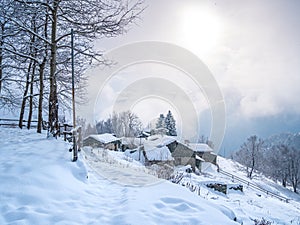 Winter in the italian Alps. Beautiful view of idyllic village in snowy forest and snowcapped mountain peaks. Piedmont, Italy