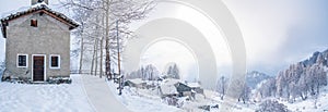 Winter in the italian Alps. Beautiful view of idyllic village in snowy forest and snowcapped mountain peaks. Piedmont, Italy