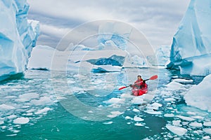 Winter kayaking in Antarctica, adventurous man paddling on sea kayak between icebergs