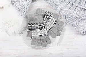 Winter knitted gloves, fur hat and pullover on white wooden background. Set of grey knitted clothes