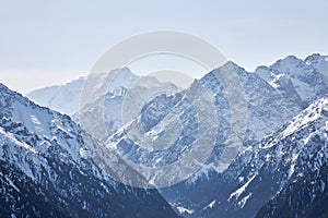 Winter in Kyrgyzstan mountains. Mountain range, snow capped peaks, border between forest and highlands