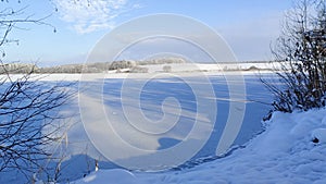 In winter, the lake is covered with ice. On the opposite shore there are snow-covered meadows and fields and frost-covered forest.