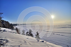 Winter lake shore with evergreen forest and sun