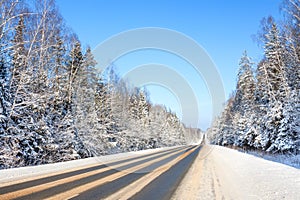 Winter landscape with asphalt road, forest and blue sky