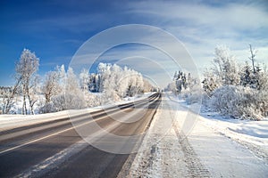 Winter landscape with asphalt road,forest and blue sky.