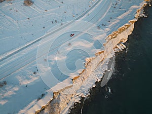 Winter landscape , drone photo. A car drives along a snowy road near a sea cliff in Paldiski