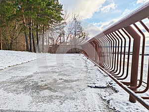 Winter landscape of the embankment by the river with a view of the forest and along the fence
