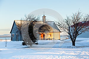 Winter landscape featuring a large grey metal barn set in fresh snow with the St. Lawrence River in the background