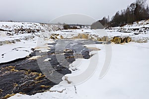 Winter landscape with a freezing river. View of the waterfall.