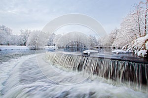 Winter landscape. Frosted trees, river, waterfall, sunlight