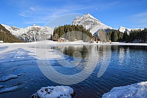 Winter landscape of the frozen Arni Lake with the snow-convered Alps peak Windgaellen