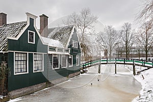 Winter landscape with frozen canal and traditional wooden house.