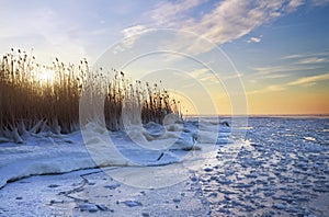 Winter landscape with frozen lake and sunset sky.