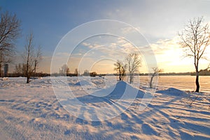 Winter landscape with frozen river covered with snow. Beautiful pink winter sunset illuminates drifts. Eco tourism