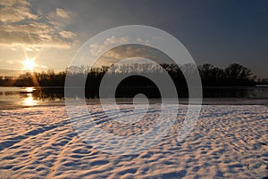 Winter landscape with frozen river covered with snow. Beautiful pink winter sunset illuminates drifts. Eco tourism