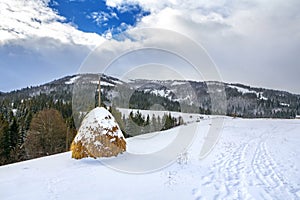 Winter landscape with a haystack on the background of snow-capped mountains and forest