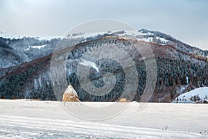 Winter landscape, a haystack on the background of snow-capped mountains and forest