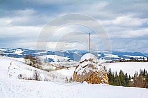 Winter landscape, haystacks on the background of snow-capped mountains and forest