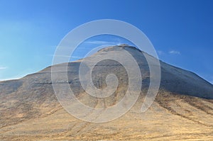 Winter landscape with a hill covered with a yellow dry grass and first snow under dark blue sky