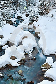 Winter landscape of a mountain river, the water slowly flows down the river bed between snow-covered stones