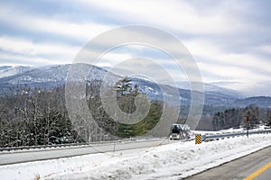 Winter landscape with mountains and forest and car hauler big rig semi truck with loaded semi trailer driving on the divided