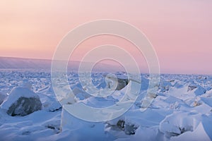 Winter landscape in pink tones with ridged ice on the frozen river at sunset