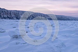 Winter landscape in purple tones with ridged ice on the frozen river at sunset