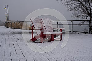 Winter landscape - red Muskoka adirondack wooden chairs in city park in heavy snowstorm