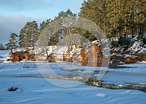 Winter landscape with red sandstone cliffs on the bank of the river Salaca, the sun shines on the trees and the river bank, the